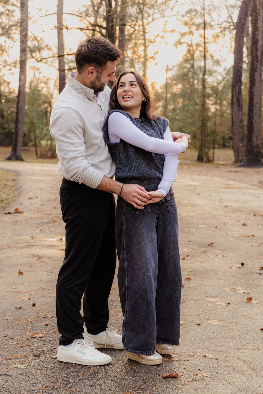 A couple sharing a romantic moment together on an autumn trail surrounded by trees at sunset.