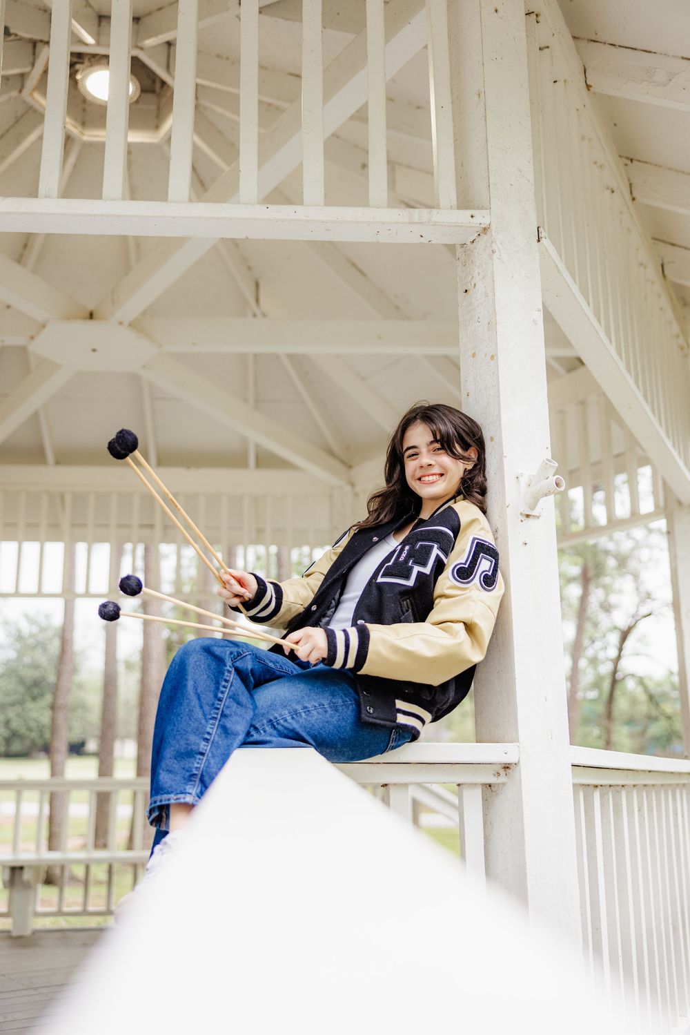 Three playful figures laying on their sides along a bright white porch railing in a casual outdoor portrait setting.