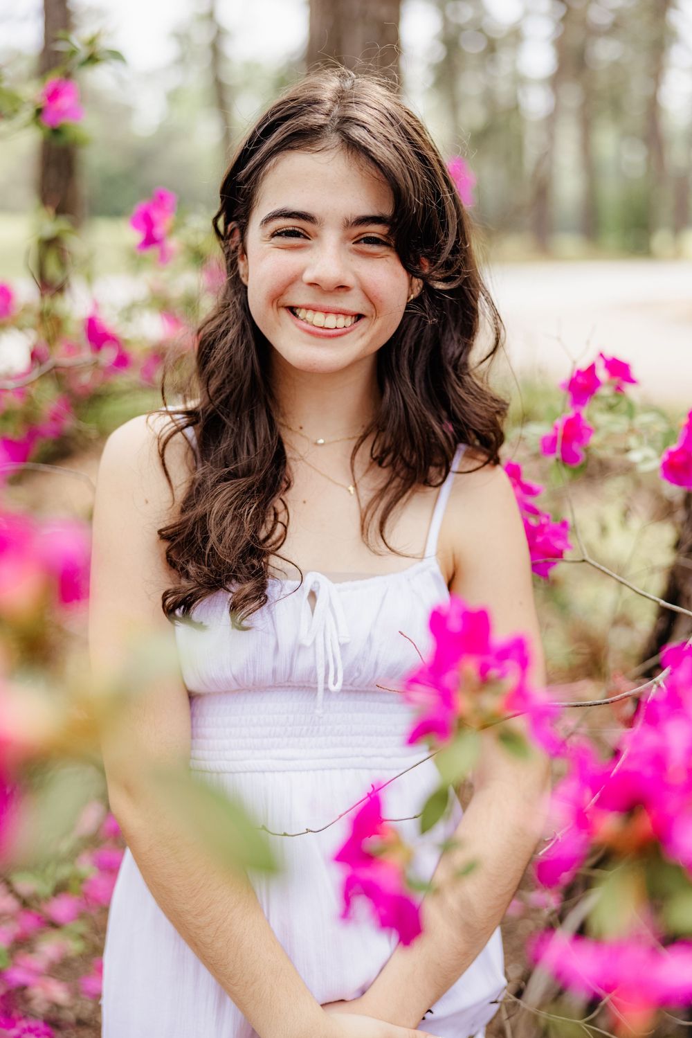 A candid portrait in a white dress among vibrant pink wildflowers in a sunlit forest setting.