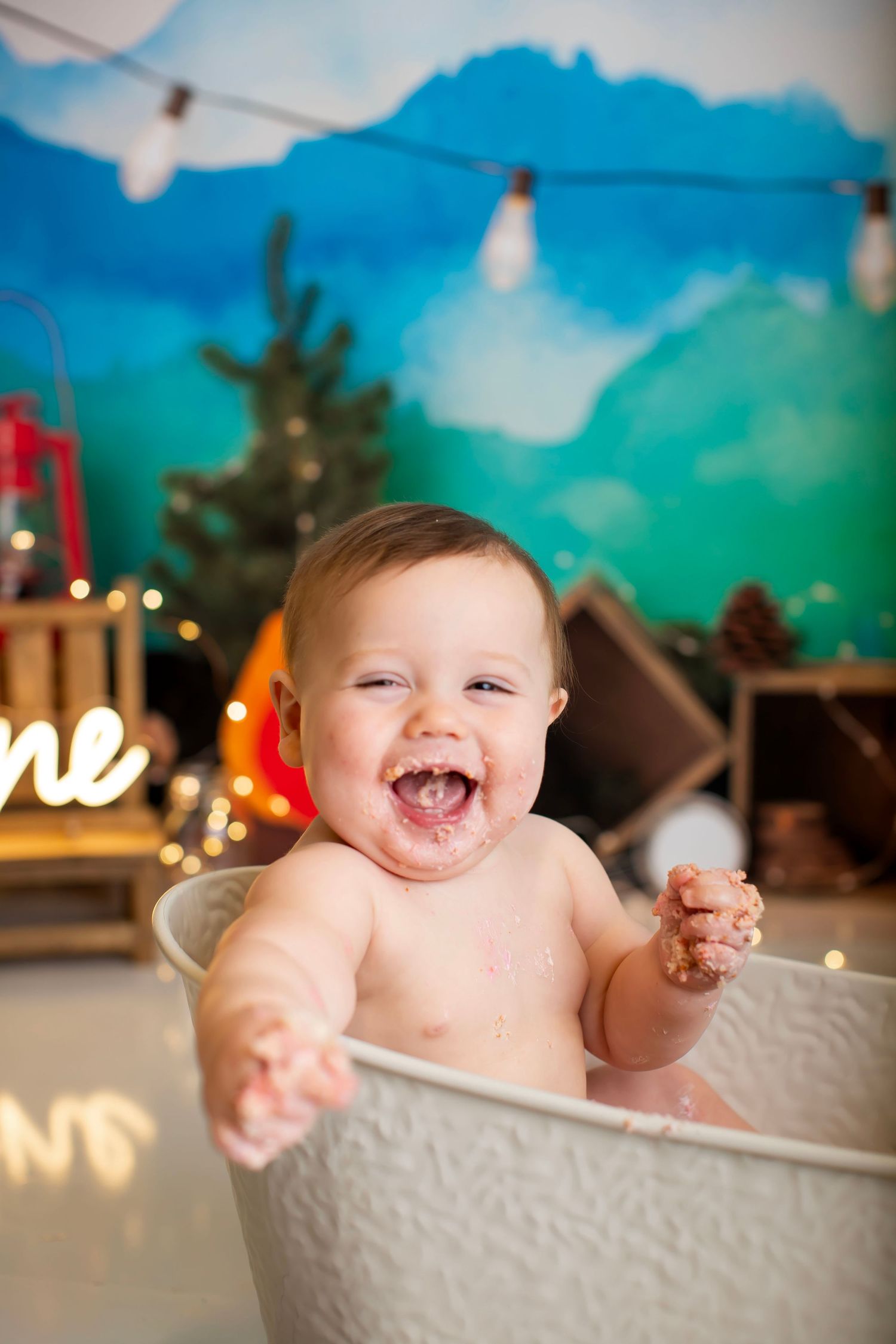 Happy baby in bathtub against mountain mural with string lights.