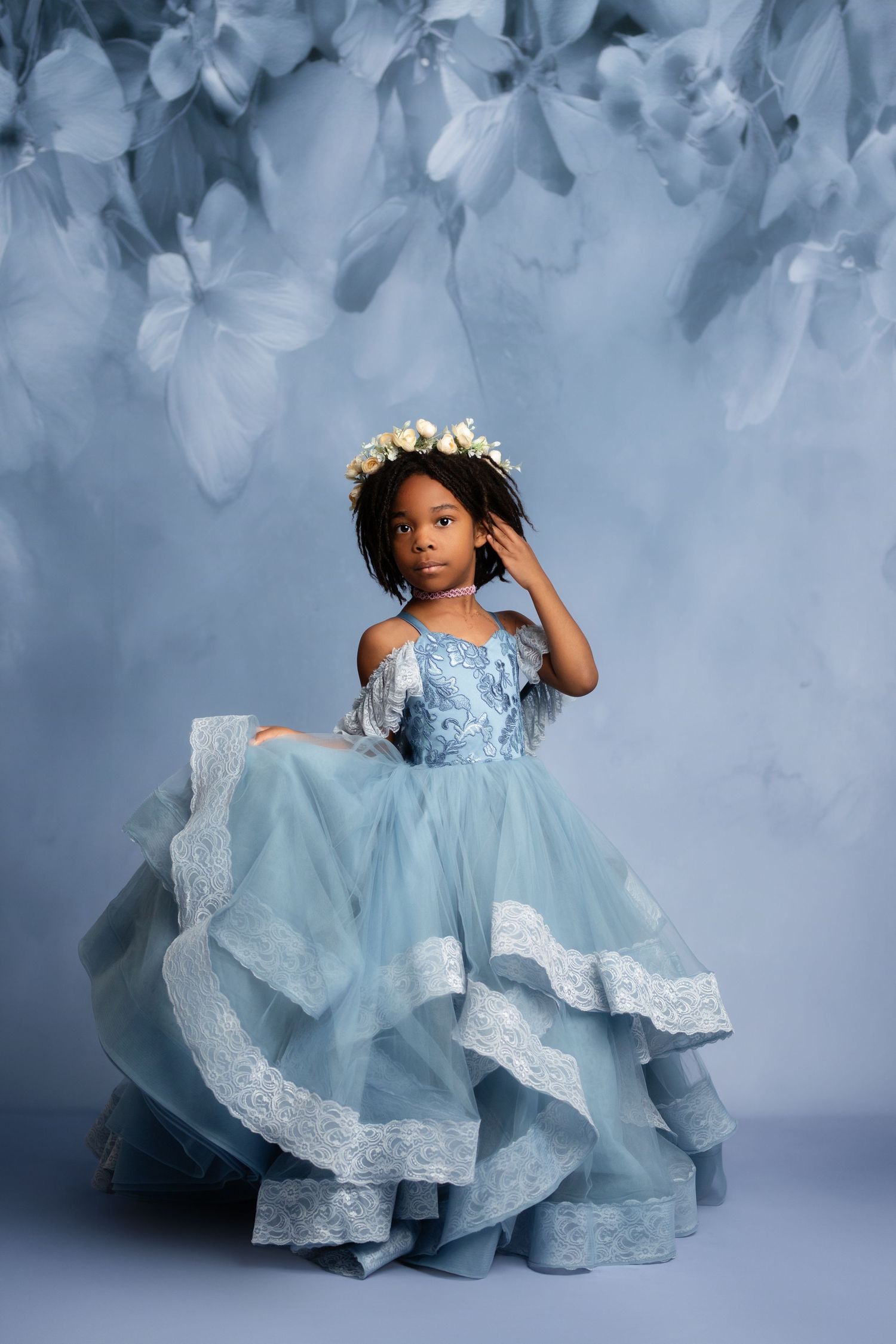 A whimsical garden portrait featuring a light blue dress with floral accents among blooming flowers.