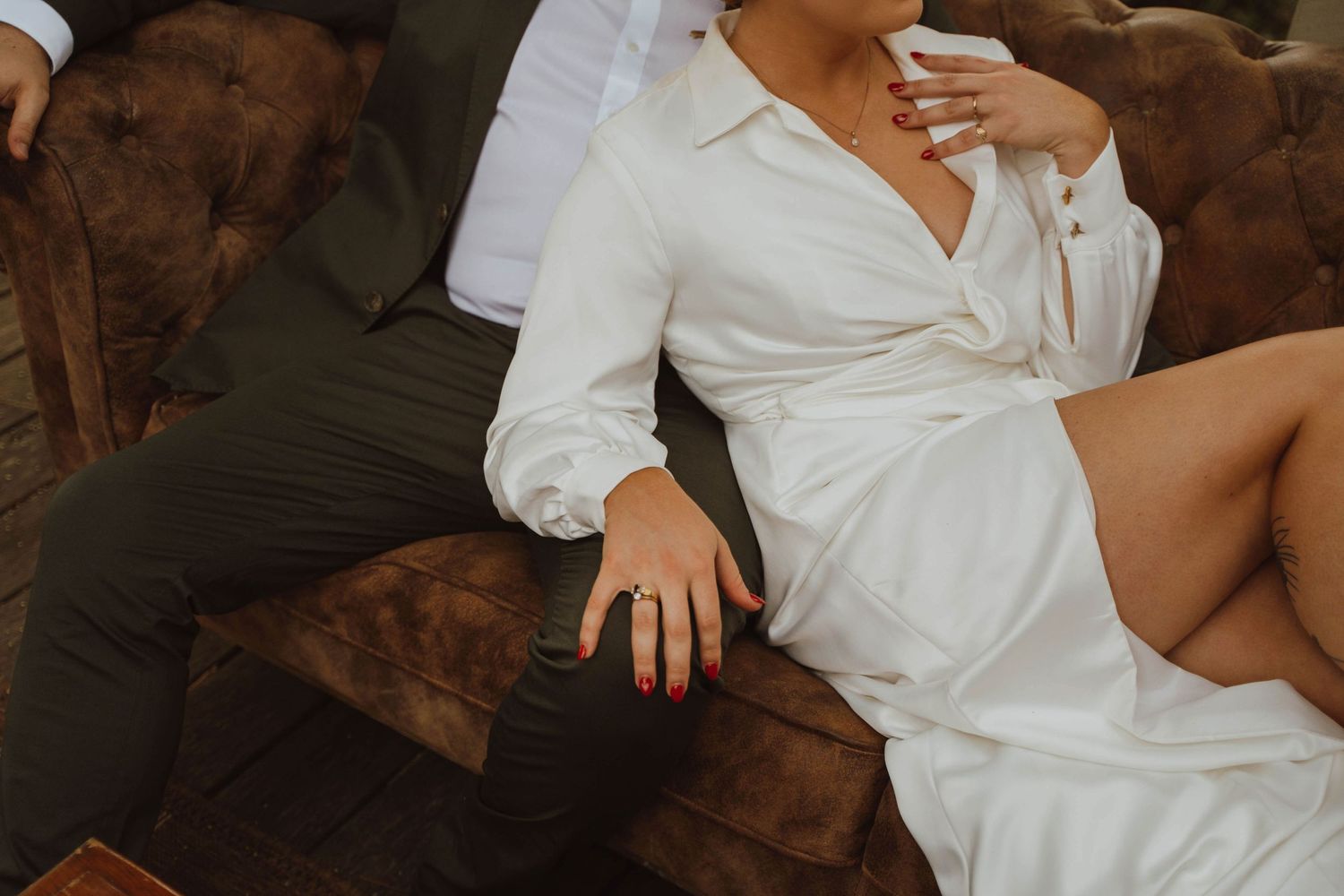 Intimate fashion photo of couple on brown velvet couch wearing white and black formal wear.