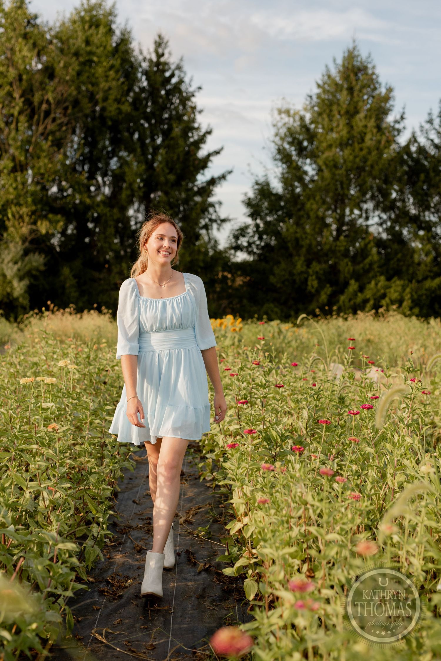 A flowing light blue dress creates a romantic silhouette on a garden path at golden hour.