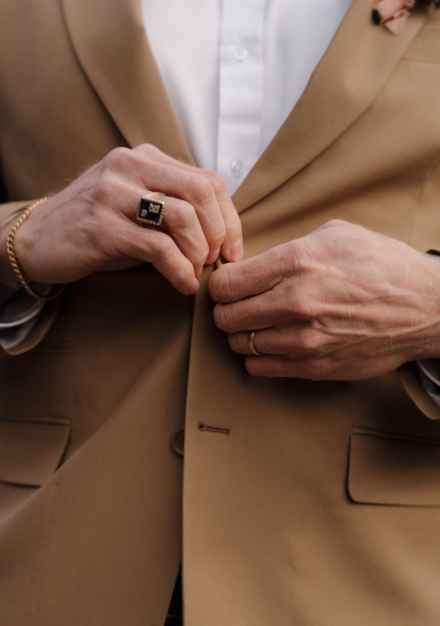 Close-up sequence showing hands buttoning a tan suit jacket pocket against a neutral background.