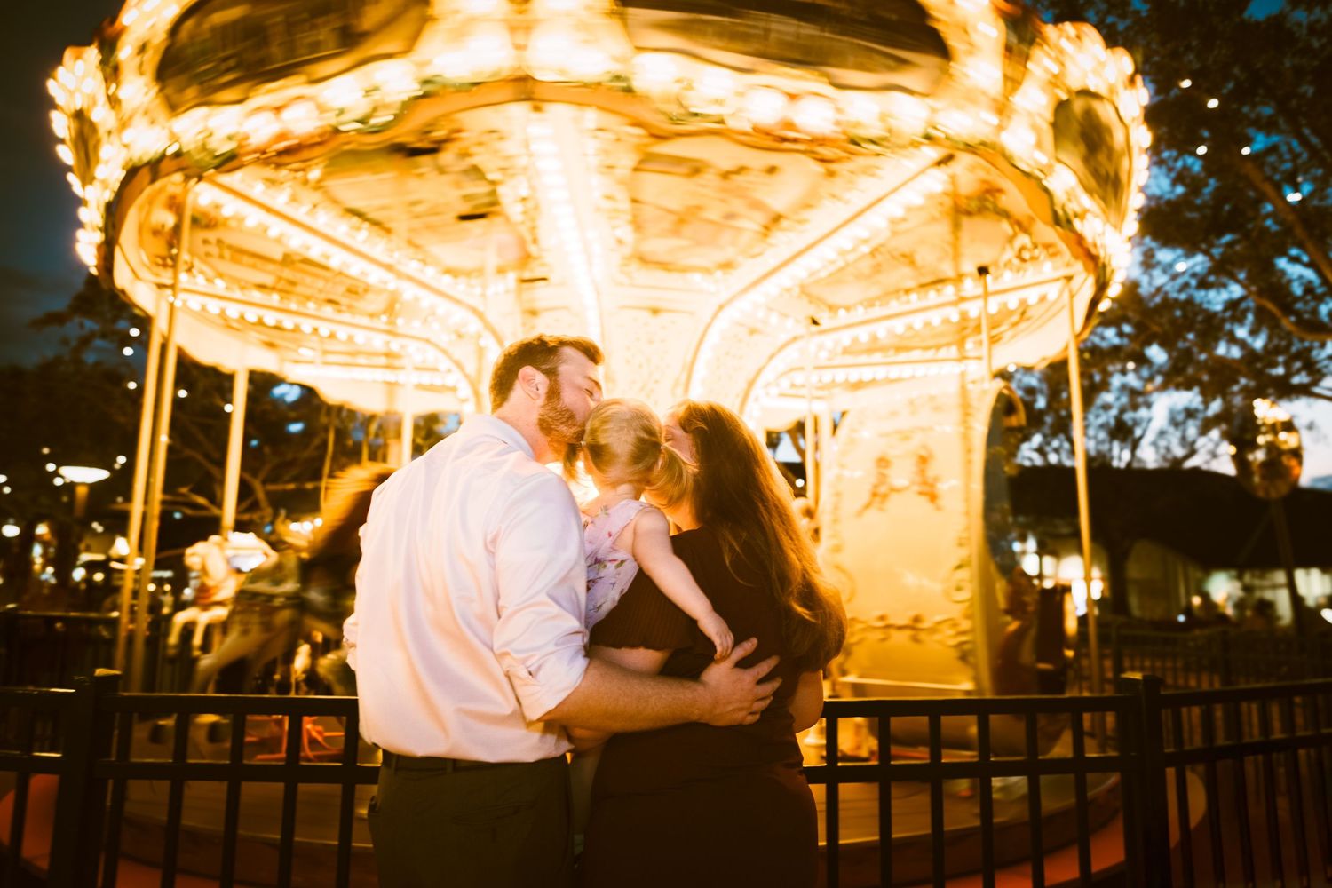 Young family in front of the Carousel at Disney Springs at Night. Cred: LexTakePix