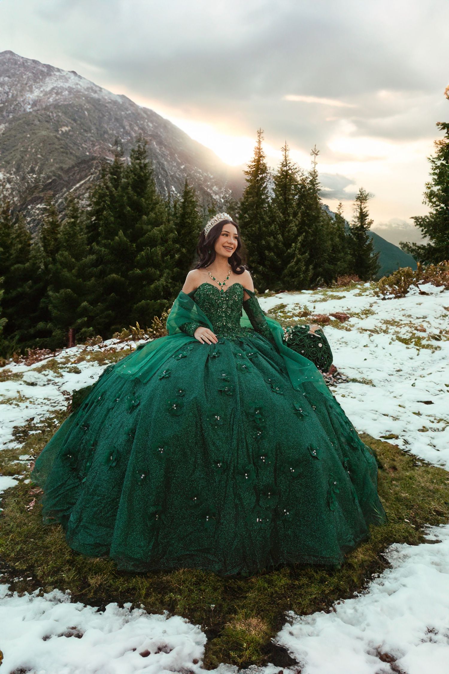 A emerald green ball gown sparkles against a snowy mountain backdrop at sunset.