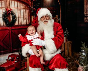 A cozy Christmas scene in a rustic barn setting with traditional holiday decorations. Santa photographer