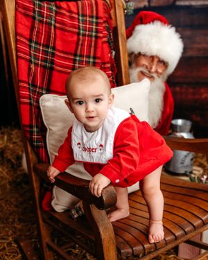 A holiday portrait in a rustic setting with plaid decorations and wooden furniture. Santa photographer