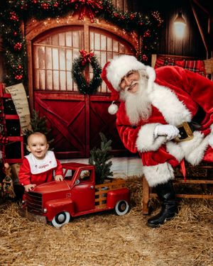 A festive barn setting with a red vintage toy truck and holiday decorations. Santa photographer