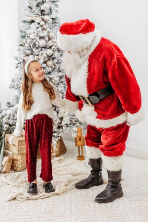 A festive Christmas scene with a decorated white tree and traditional red and white holiday outfits. Santa photographer