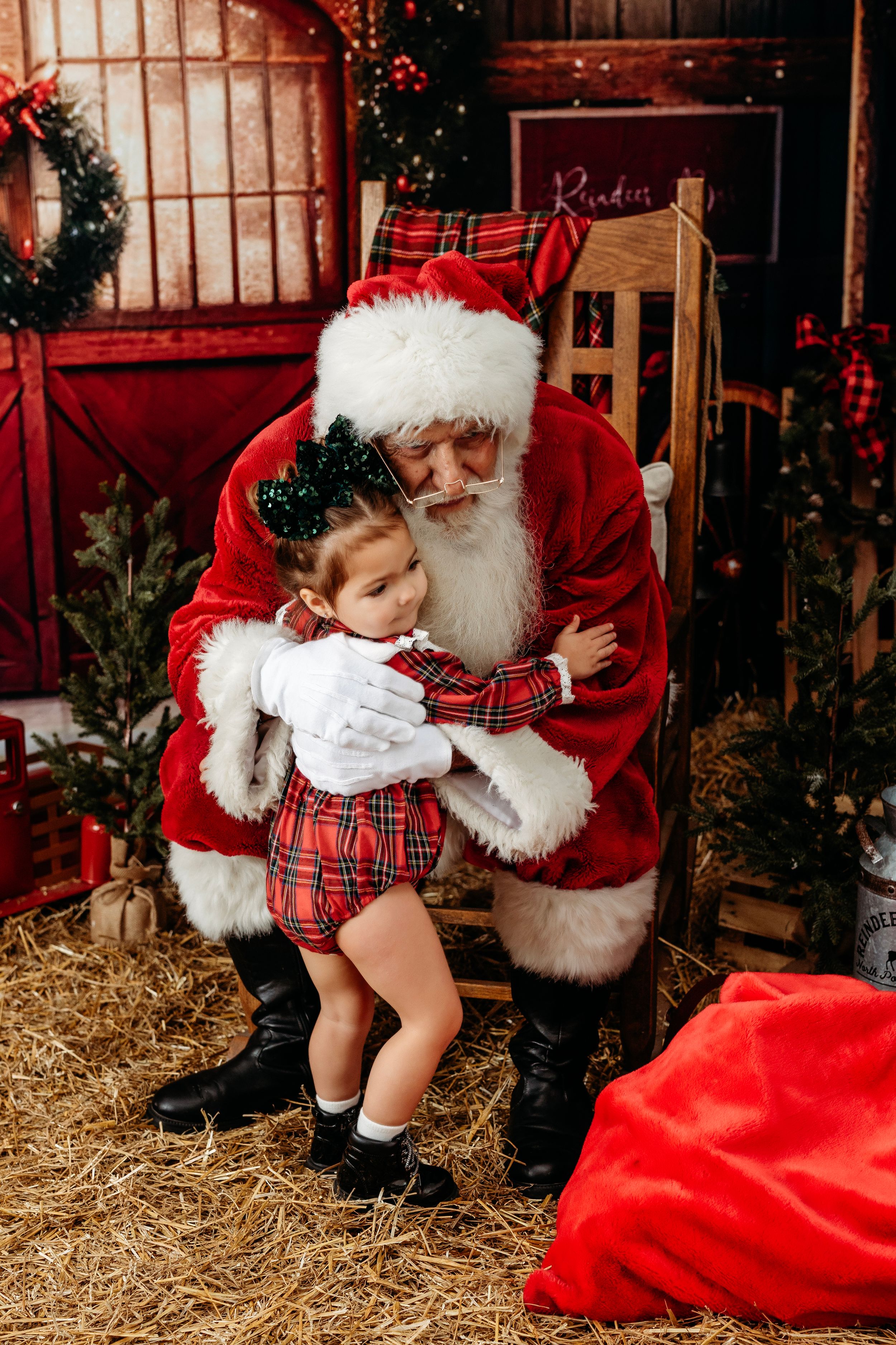 Holiday portraits in rustic barn setting with hay and red Christmas decorations. Santa photographer