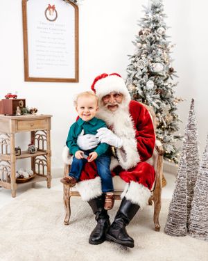 A festive Christmas photo session setup with decorated trees, a wooden chair, and white winter decor. Santa photographer