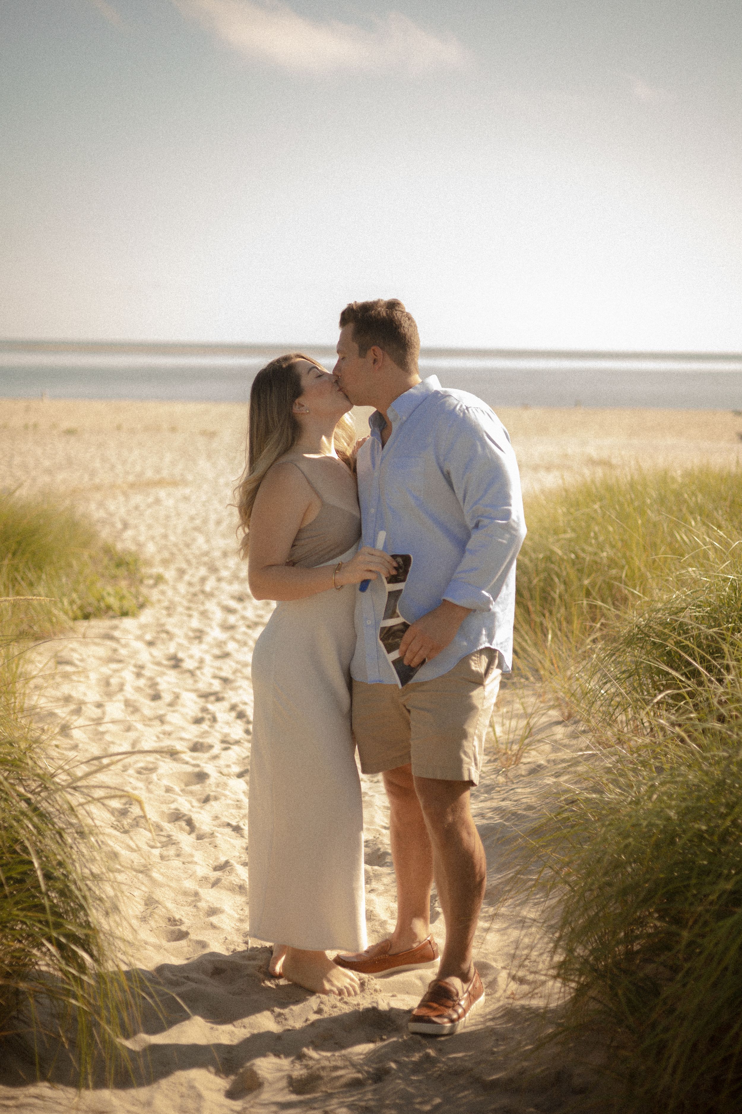 A romantic moment between a couple standing on a sandy beach path surrounded by dune grass.