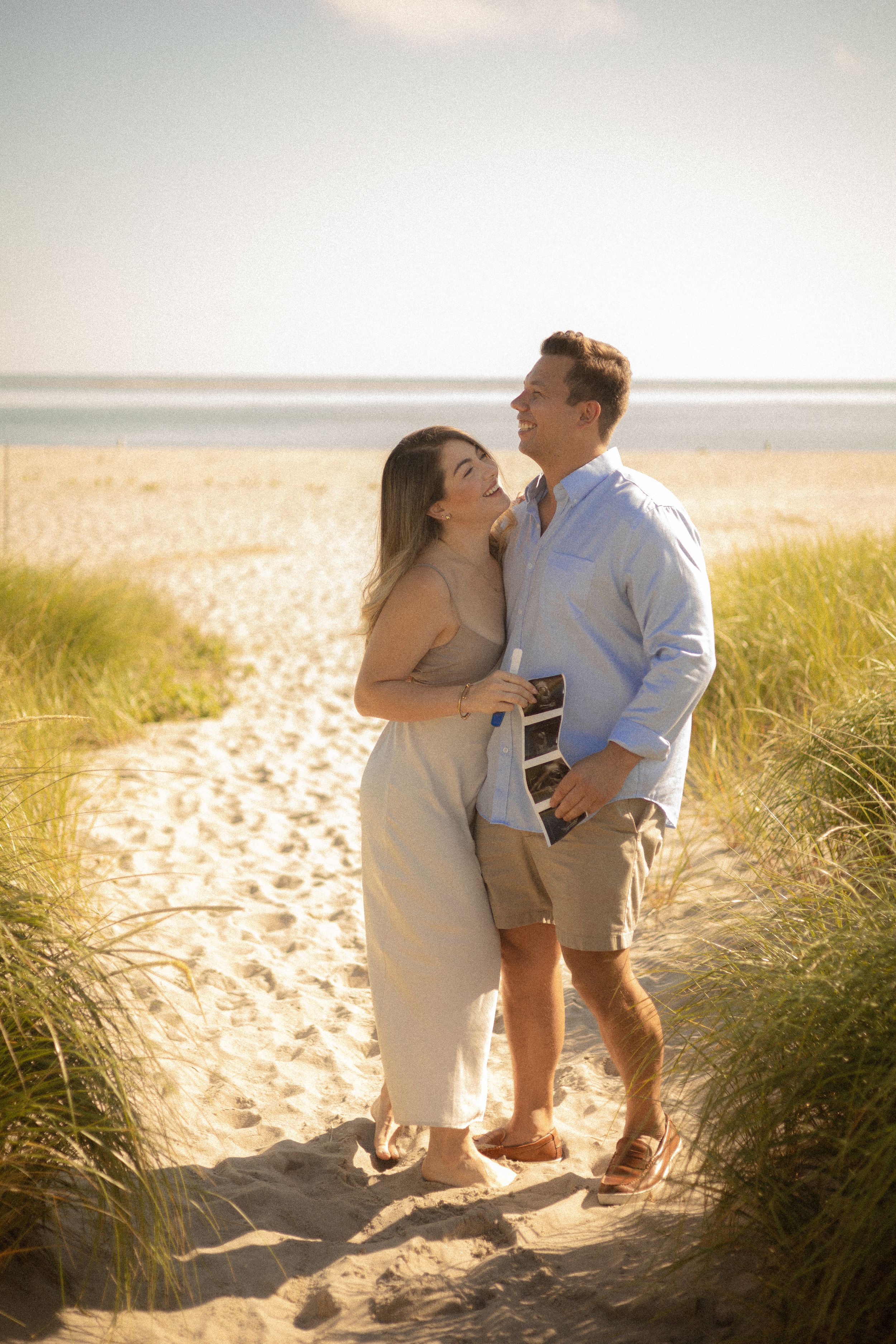 Couple embracing on sandy beach path during golden hour.