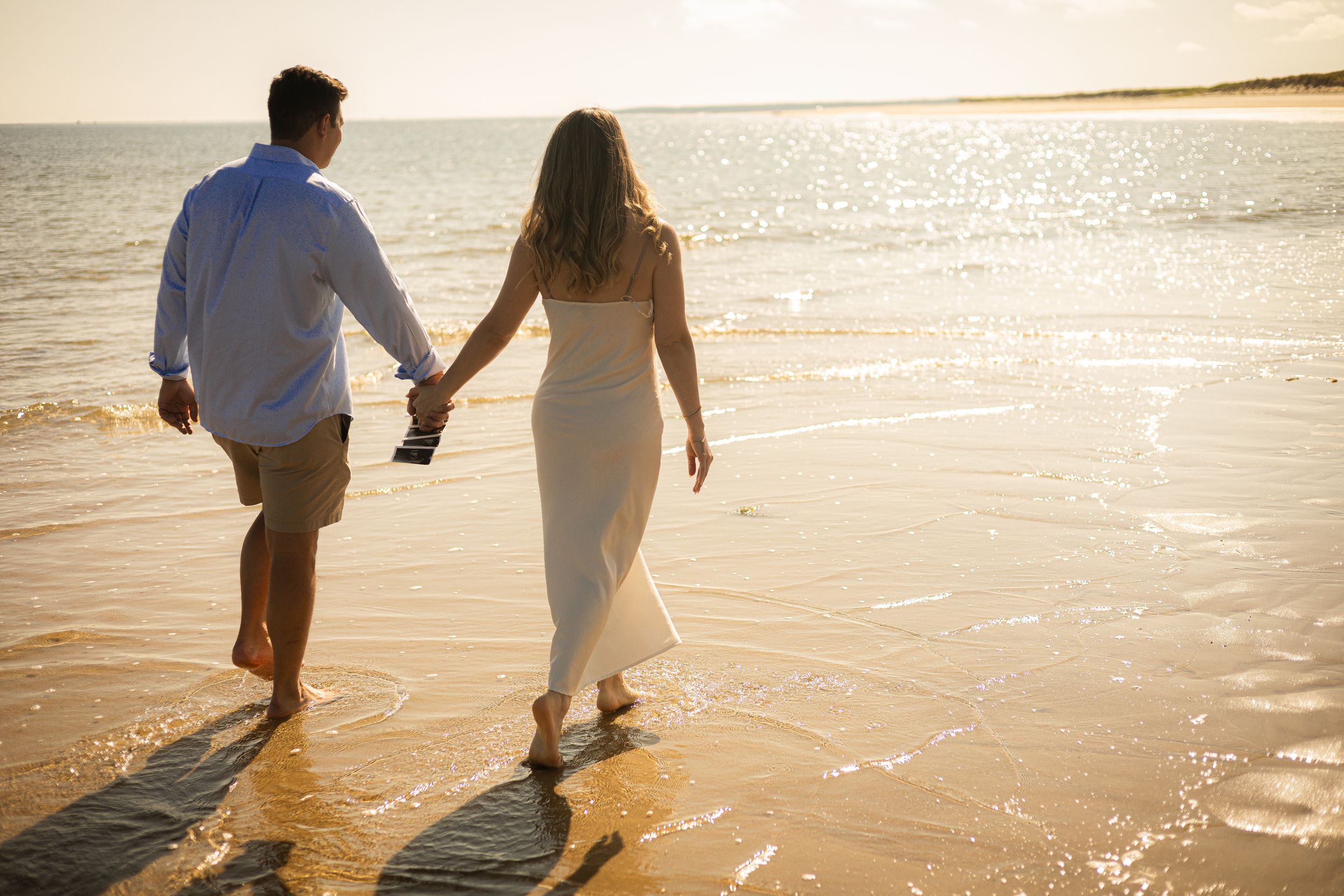 Couple walking hand in hand along shoreline during sunset.
