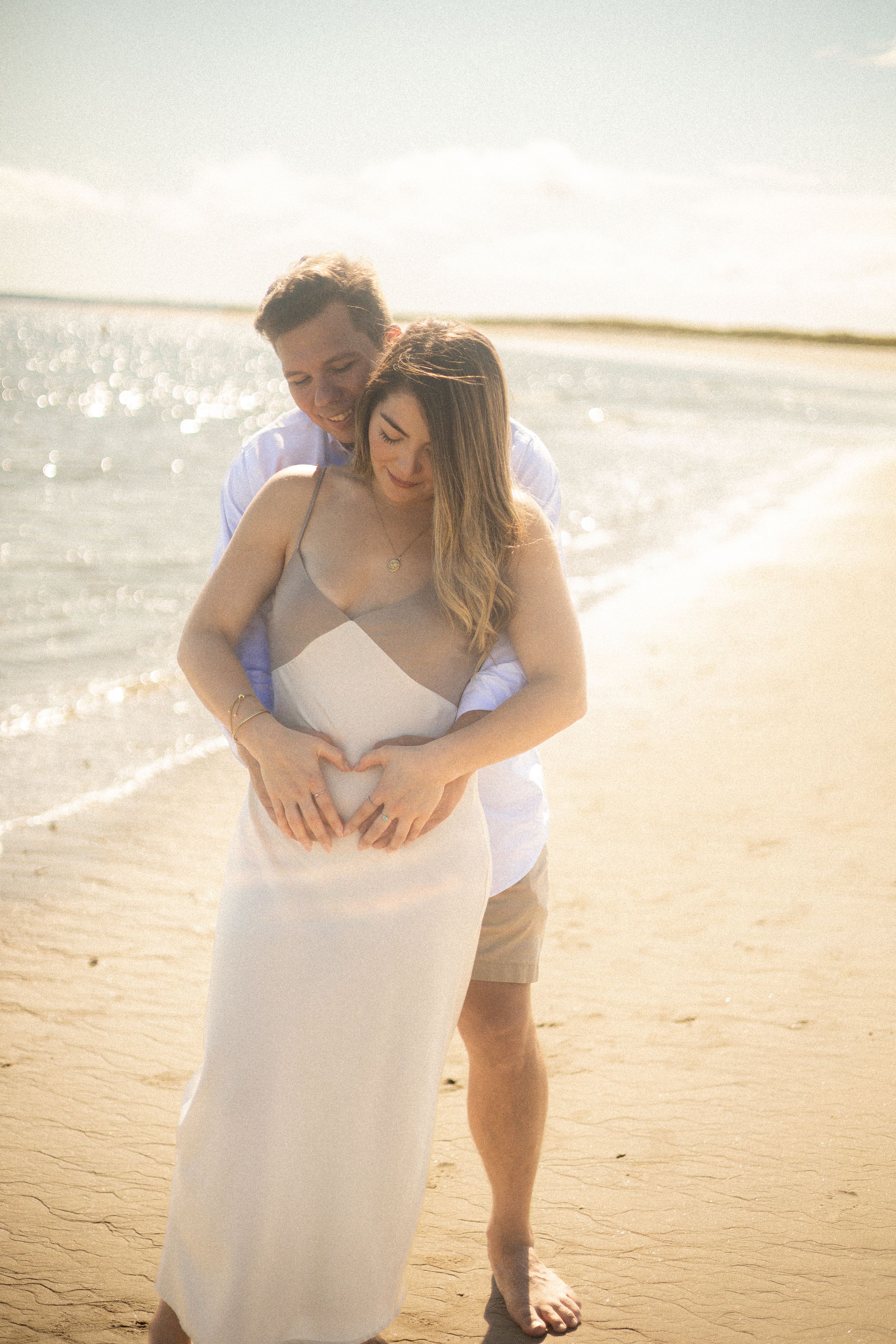 A tender embrace between a couple on a sandy beach with sparkling water in the distance.