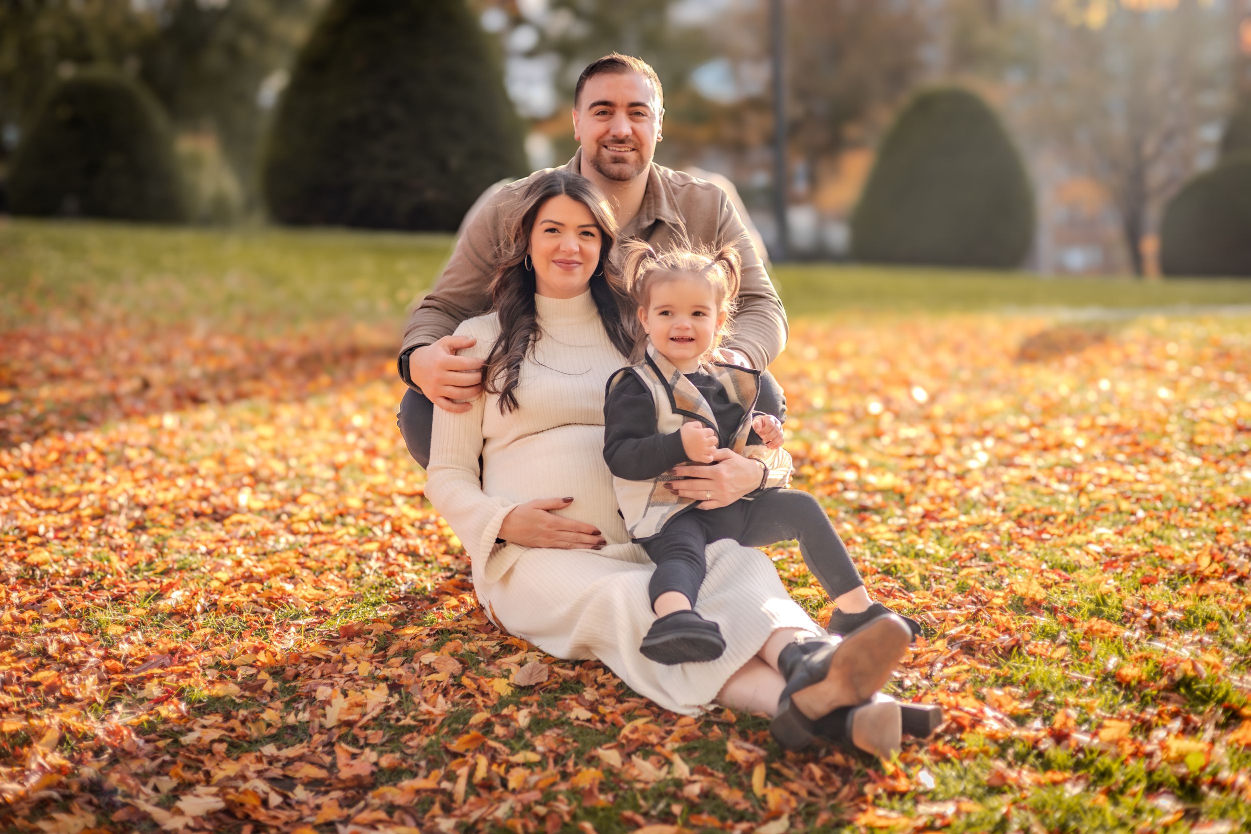 Happy family sitting together on autumn ground covered in orange fallen leaves in a park.