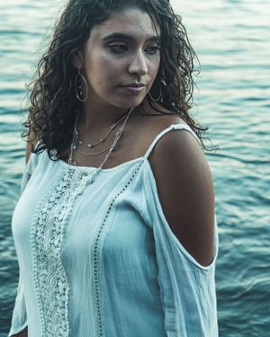 Coastal portrait in white lace dress against blue ocean background.