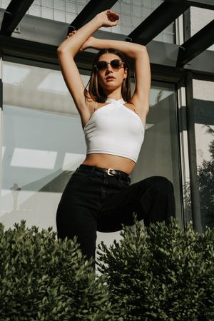 Fashion model in white crop top and black pants poses against modern architecture with dramatic lighting.