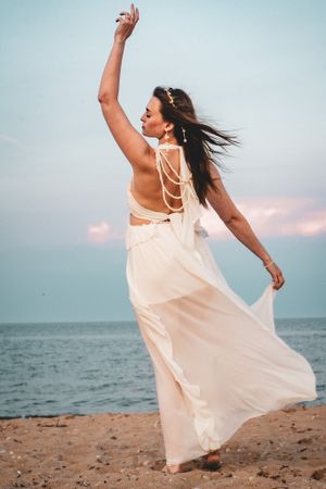 Flowing white dress catches wind as dancer poses gracefully on beach at sunset.