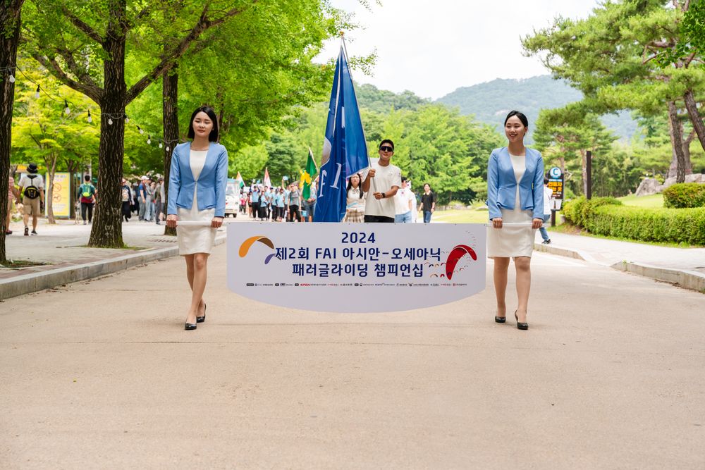 Participants carry a blue banner at an outdoor event along a tree-lined path.
