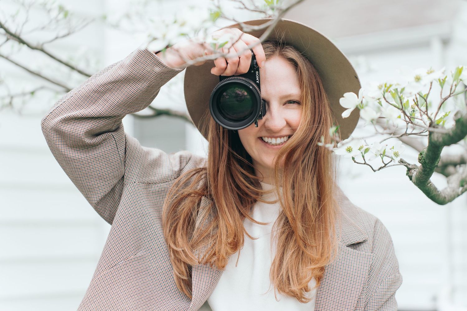 Photographer in beige coat with camera smiling among spring blossoms. Cuyahoga Falls, Ohio