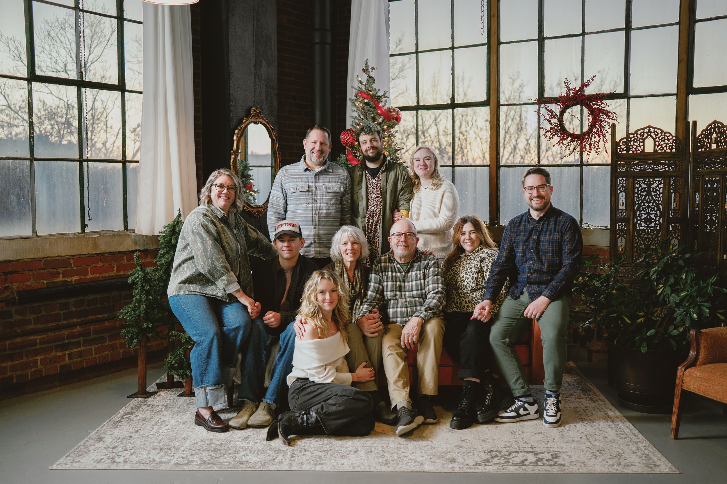 Family group portrait in a bright sunroom with large windows, brick walls, and indoor plants at Akron Photo Society for family photos.