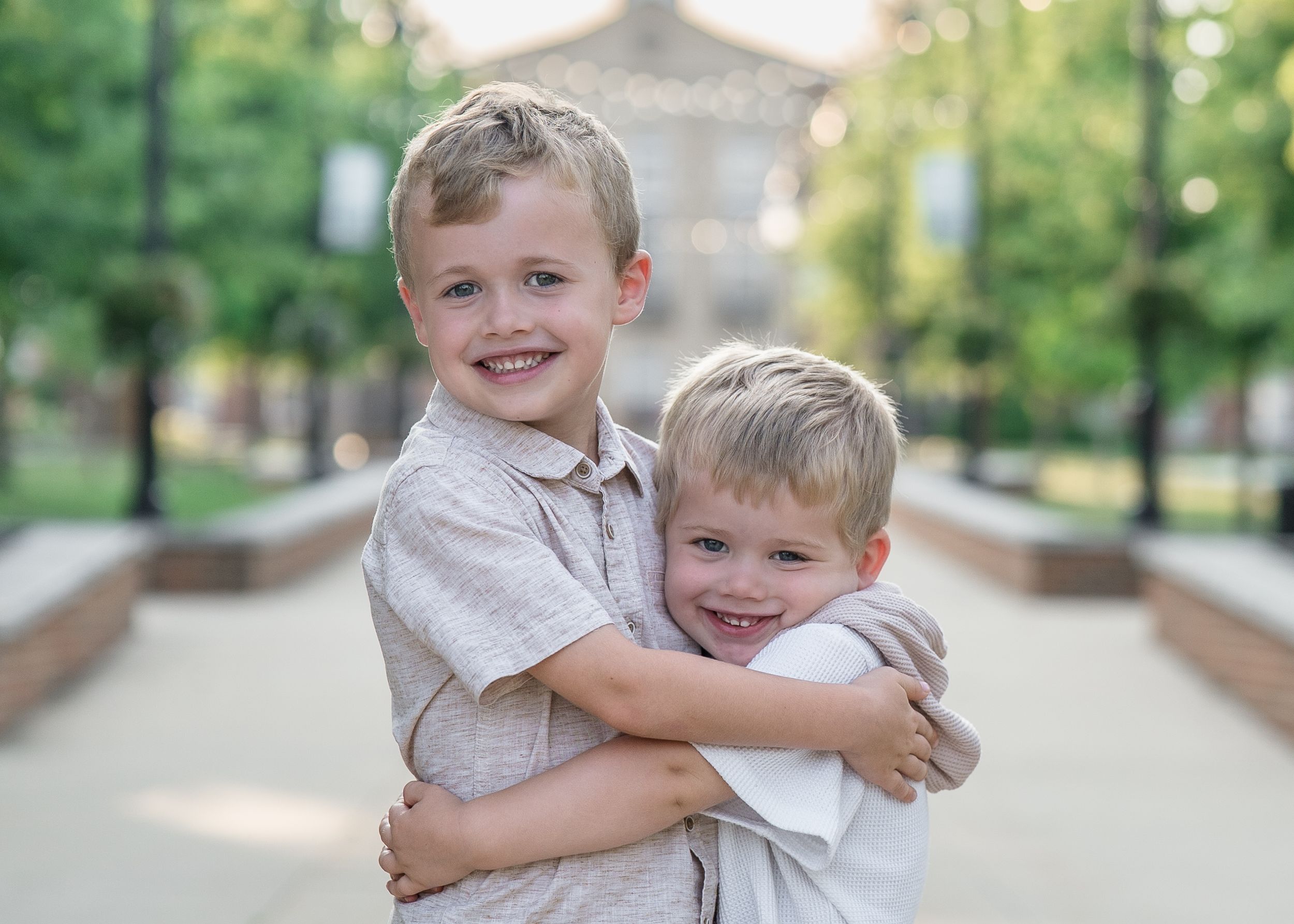 Two young children in light colored shirts share a warm embrace while standing on a walkway with a blurred downtown Cuyahoga Falls, Ohio pic