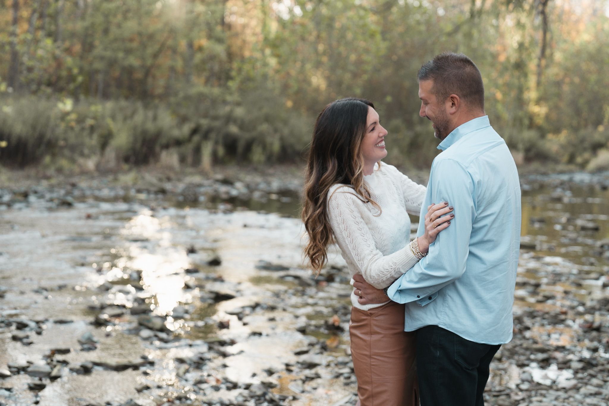 A couple shares romantic moments along a creek in a natural wooded setting during their engagement photo session at Brecksville Reservation