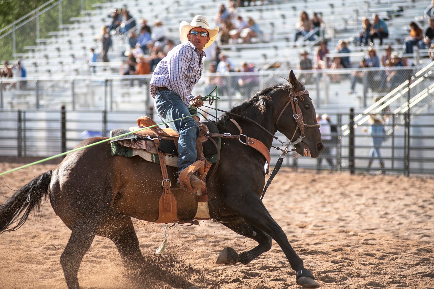 Action shot of rodeo rider on horseback competing in dusty arena with spectators.