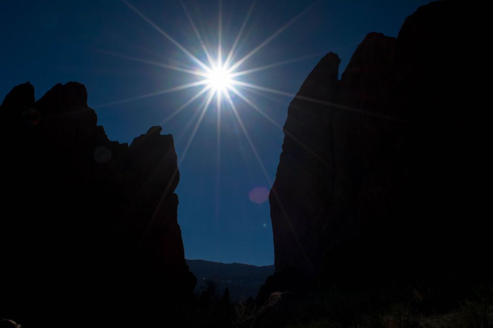 Bright sunburst between silhouetted rock formations against deep blue sky.
