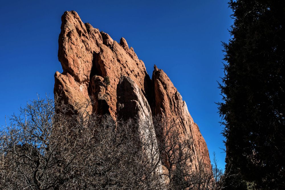 Towering red rock formation rises against bright blue sky in Garden of the Gods, Colorado.