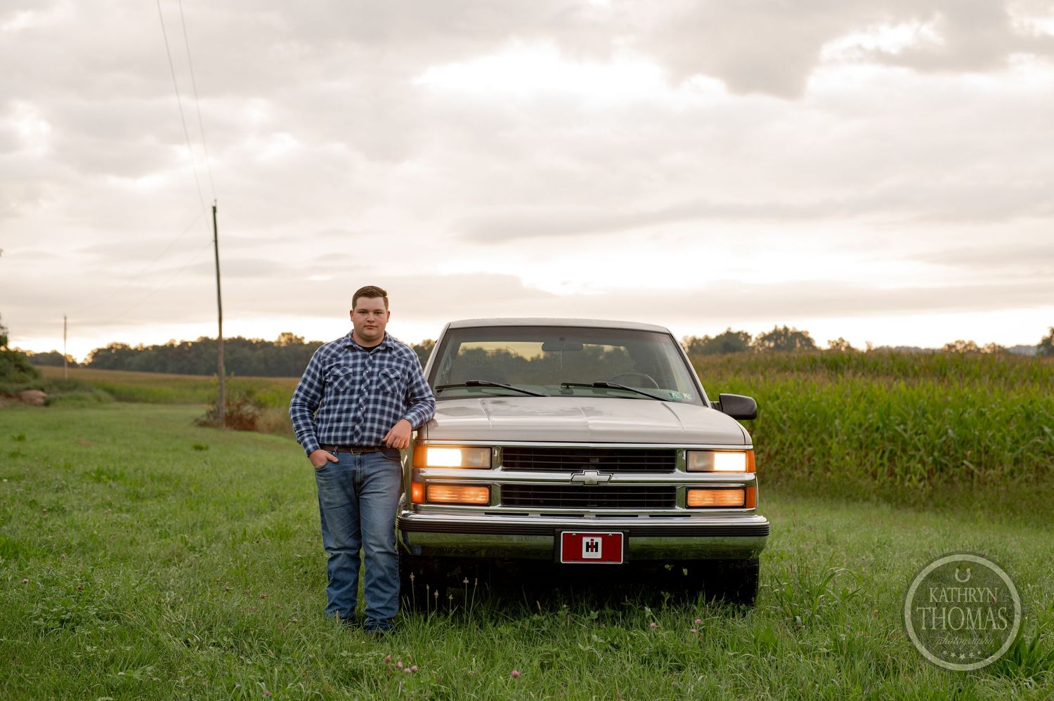 A person stands in front of a silver Chevrolet pickup truck in a rural field setting.