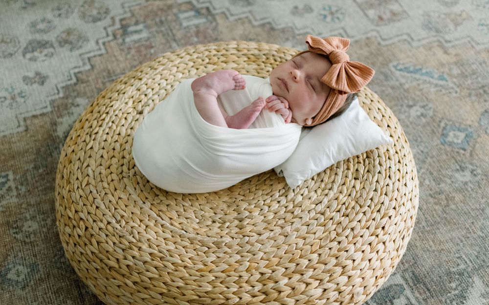 Newborn baby dressed in white photographed on round woven natural fiber mat.