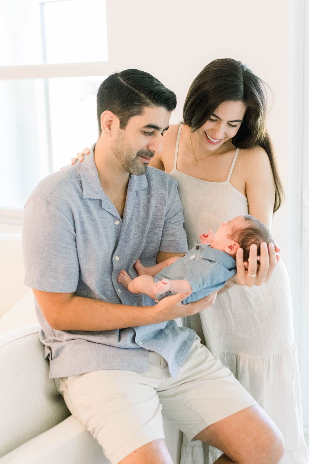 New parents sharing tender moment with their newborn baby in bright, minimalist setting.