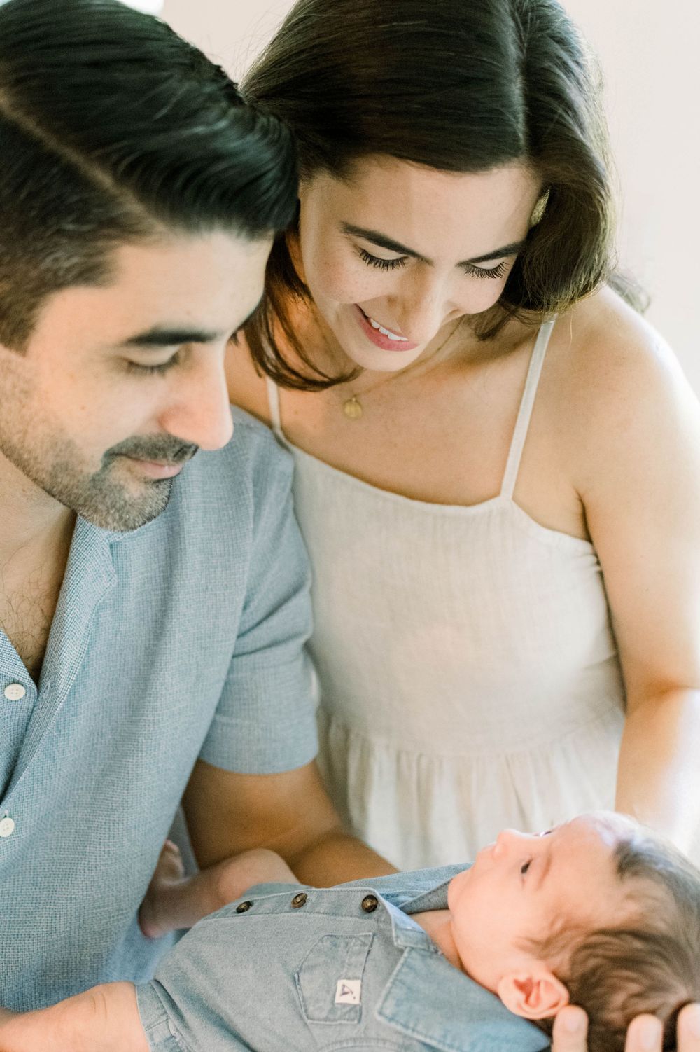 Intimate lifestyle portrait of new parents gazing lovingly at their baby in natural light.