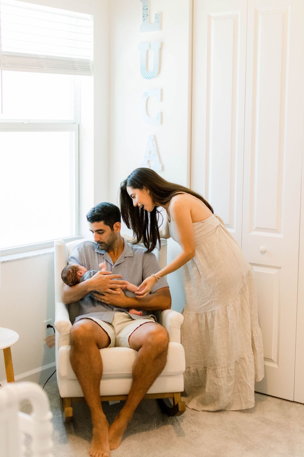 New parents bonding with their infant in a cozy white nursery corner.