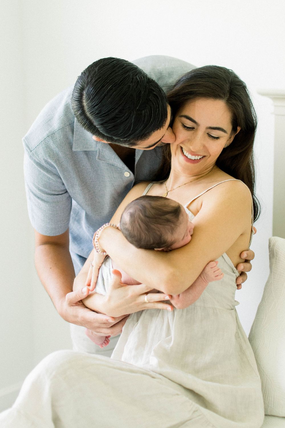 Intimate family portrait showing tender moment with newborn in bright white setting.