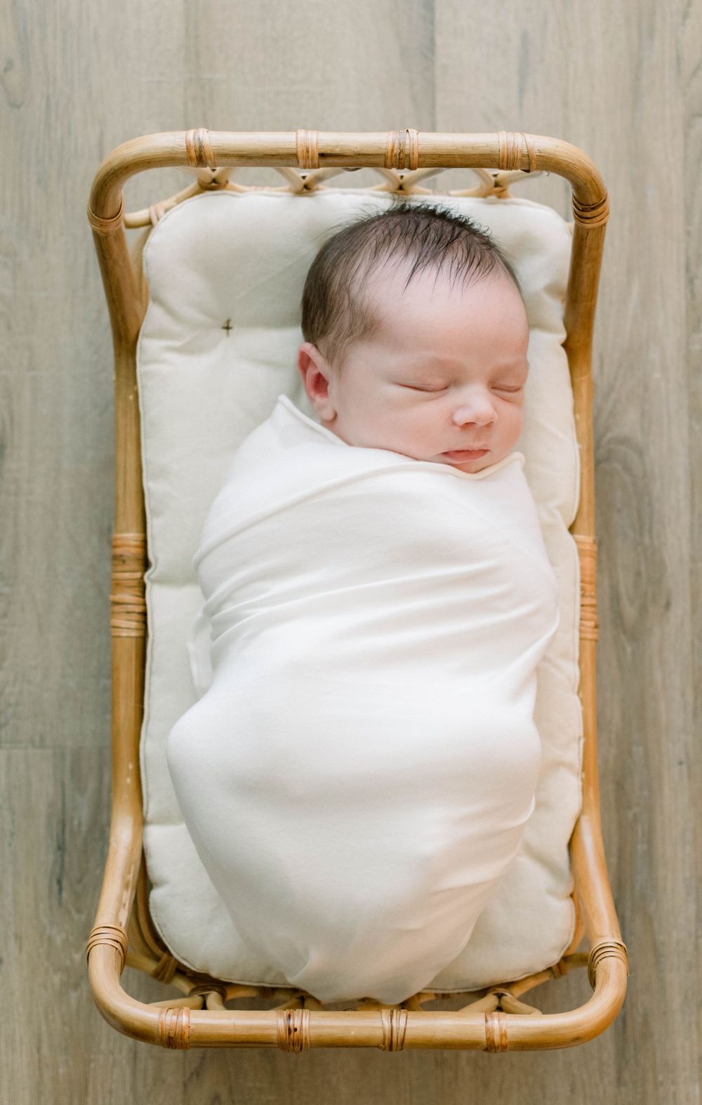 Sleeping newborn wrapped in white lying in a bamboo bassinet.