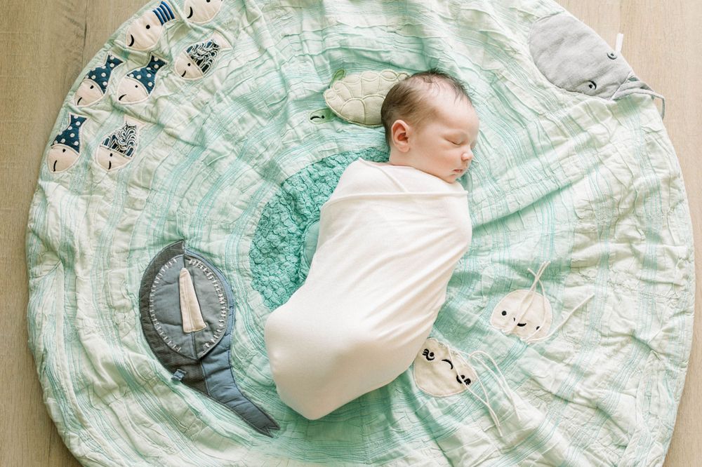 Swaddled newborn sleeping on a patterned turquoise blanket with moon designs.
