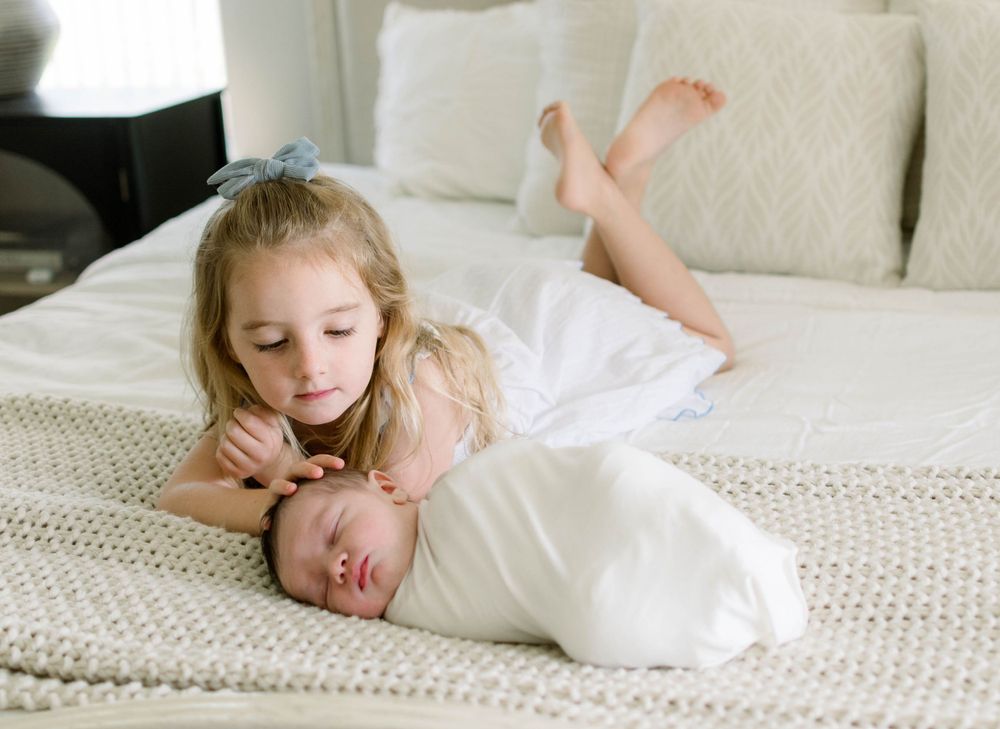 A tender moment between two siblings on a white bed with textured bedding.