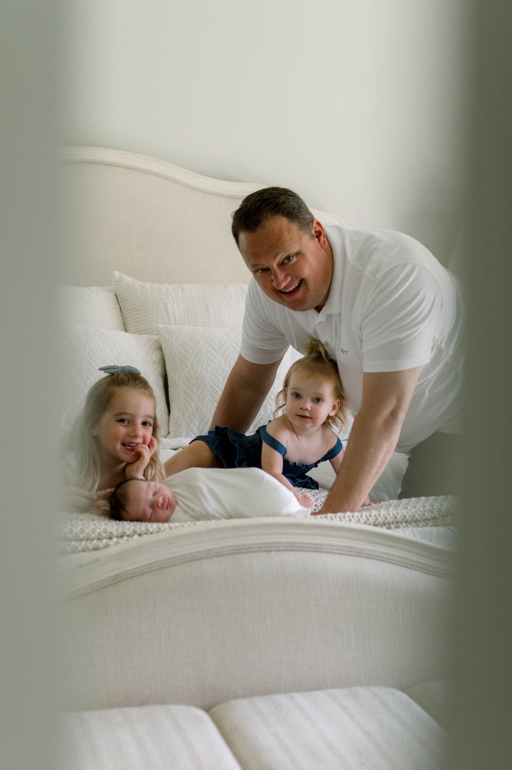 Candid family moment captured through window reflection on white bedding.