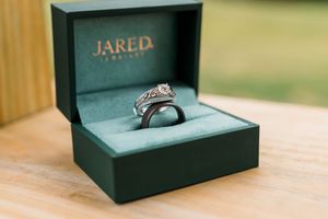 Diamond engagement ring set in a green Jared Jewelers box displayed on a wooden surface.