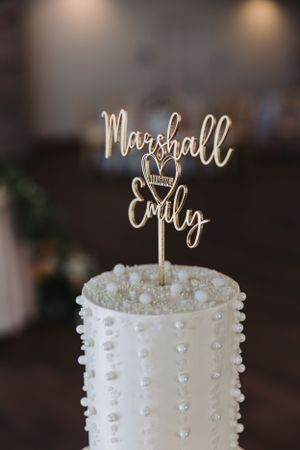 White wedding cake decorated with delicate pearls and custom script topper.