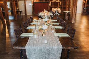 Elegant reception hall with long dining tables set under rustic wooden beams.