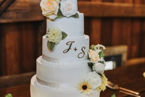 White tiered wedding cake adorned with roses and sunflowers.