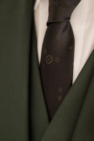 Close-up detail of dark patterned tie against white shirt and green suit jacket.