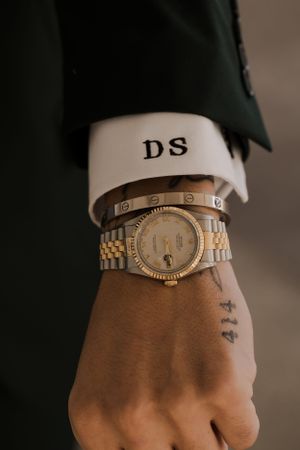 Luxury watch and monogrammed cuff detail on formal suit sleeve.