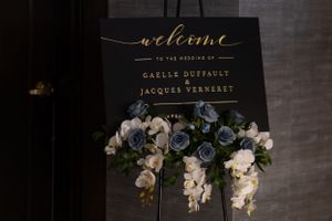 Elegant wedding welcome sign with gold calligraphy and white floral arrangements.