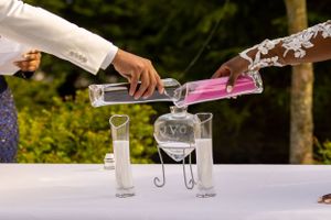 Two hands pouring colorful sand into clear vessels during a unity ceremony at a wedding.